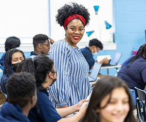 A teacher stands in a room of students smiling
